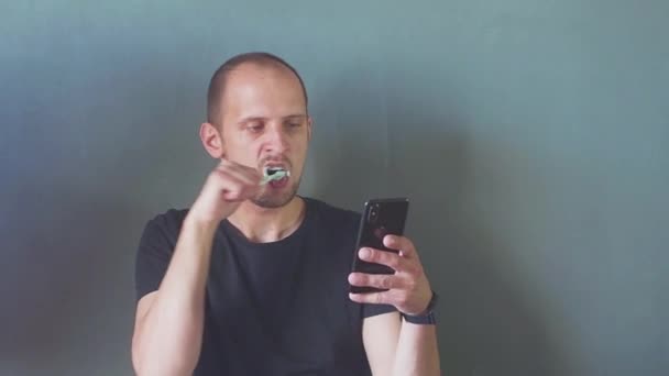 Close up de homem usando smartphone. conceito de vício em telefone. jovem homem de negócios digitando e navegando mídias sociais em seu telefone enquanto escova os dentes. Hd — Vídeo de Stock
