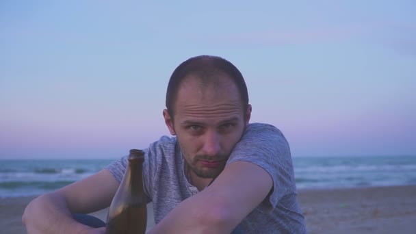 Ubriaco che beve birra sulla spiaggia di mare la sera. Ritratto di un uomo che beve birra da una bottiglia — Video Stock