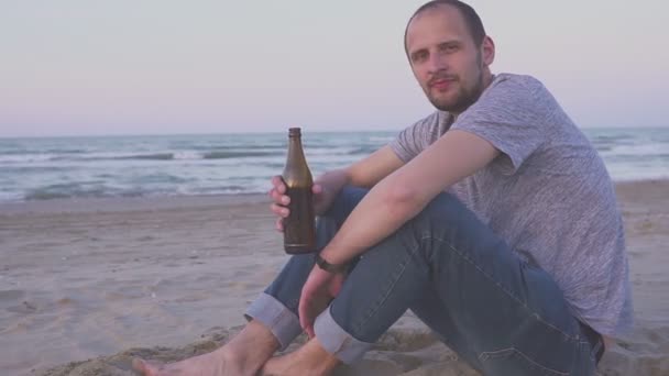 П'яний чоловік п'є пиво на морському пляжі ввечері. Портрет чоловіка, який п'є пиво з пляшки — стокове відео