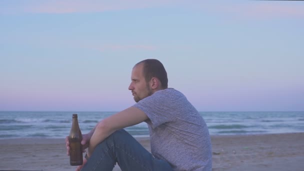 夕方には海のビーチでビールを飲む男を飲む。瓶からビールを飲む男の肖像 — ストック動画