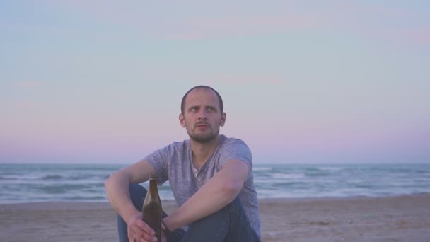 Homme ivre buvant de la bière sur la plage de la mer dans la soirée. Portrait d'un homme buvant de la bière dans une bouteille — Video