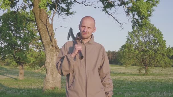 Porträt eines Mannes, der mit einer Axt in der Hand auf dem Feld steht... Typ mit Axt im Freien. — Stockvideo