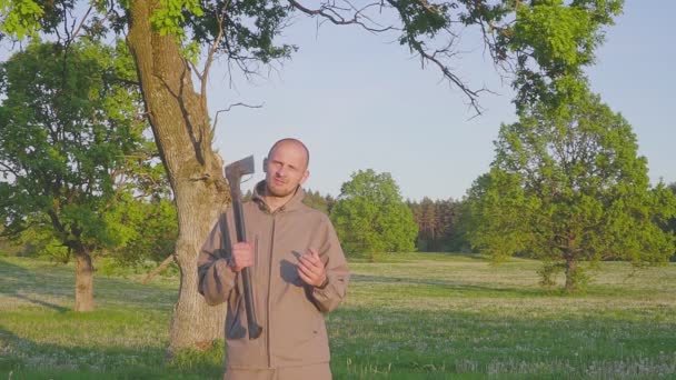 Portret van een man staande met een bijl in zijn hand in het veld... man met AX buitenshuis. — Stockvideo