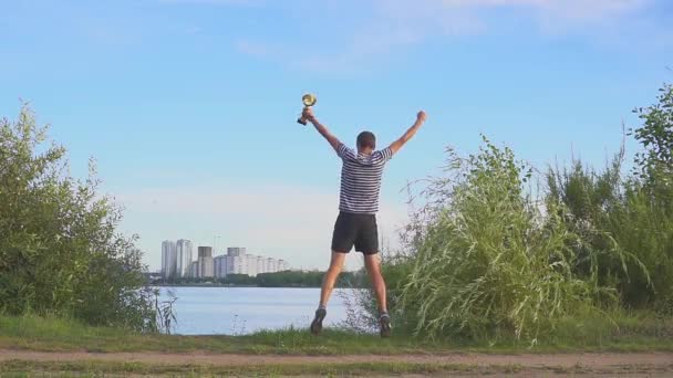 Ένας νέος άντρας με ένα φλιτζάνι στα χέρια του χαίρεται στη νίκη του αθλητισμού στο παρασκήνιο της βραδιάς Μινσκ. Concept ως νίκη, επιτυχία και πρωταθλητής στον αθλητισμό. Αργή κίνηση. Μινσκ 2019. — Αρχείο Βίντεο