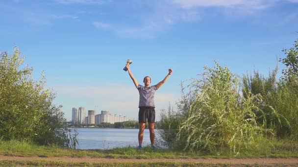 Egy fiatal férfi egy csésze kezével örvendő a sportgyőzelem a háttérben az esti Minszk. Koncepció, mint a győzelem, a siker és a bajnok a sportban. Lassított. Minszk 2019. — Stock videók