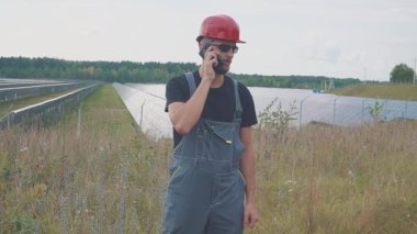 Yakınındaki bir güneş güç istasyonu ve jestleri, telefonda konuşan işçinin portre pozitif sinyaller yapar