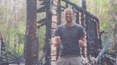 Yanmış bir evin arka planında üzgün bir adamın portresi, yangından sonra. Yangın felaketkazasının sonuçları. Yangın felaketinden sonra harabeler, umutsuzluk kavramı.