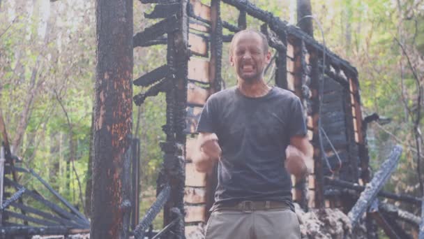 Retrato de un hombre triste en el fondo de una casa quemada, después del fuego. Consecuencias del accidente de incendio. Ruinas después del desastre de fuego, concepto de desesperación . — Vídeos de Stock