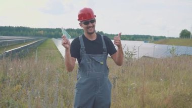 Bir güneş enerjisi istasyonunda çalışan ya da mühendis. Elinde euro banknotları tutuyor, parasını anlatıyor. Gülümseyin ve tamam imzalayın, gibi.