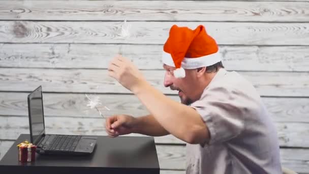 Bonito homem com símbolo de Papai Noel está usando um laptop e se alegra com fogo brilhante — Vídeo de Stock