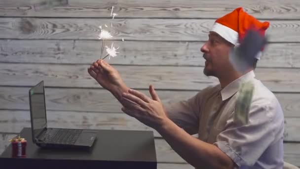 Marzycielski człowieka w Boże Narodzenie kapelusz z Bengalu ogień brylant i laptopa w jego ręce. Spadające ceny dolarów. — Wideo stockowe