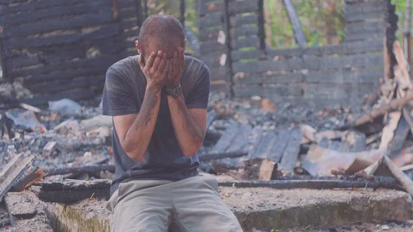 Portrait of a sad man on the background of a burned house, after fire . Consequences of fire disaster accident. Ruins after fire disaster, despair concept. Stock Picture