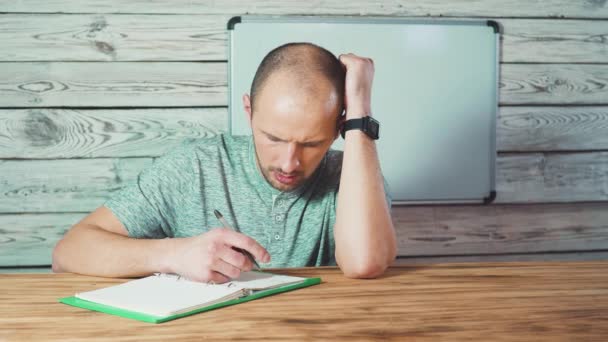 Tipo barbudo pensativo escribiendo en las ideas del bloc de notas, soñando sonriente estudiante masculino en gafas mirando hacia otro lado haciendo notas . — Vídeos de Stock