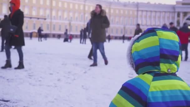 Retrato de niño mirando a la cámara con cara curiosa, Niño Activo con sombrero de lana y bufanda. Mucha gente detrás. Invierno San Petersburgo — Vídeos de Stock