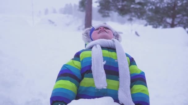 Retrato de un niño feliz en el bosque de invierno apoyado agaist un tronco de árbol, la luz de la tarde baja, bokeh en el fondo. luz nocturna . — Vídeo de stock