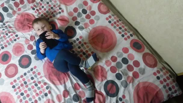 Kind liegt auf dem Bett und blickt auf ein elektronisches Smartphone-Display — Stockvideo
