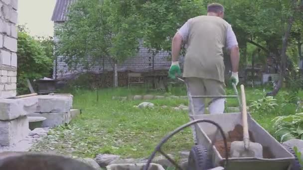 Gardener man with wheelbarrow going countryside road garden backyard. Hard physical labor — Stock Video