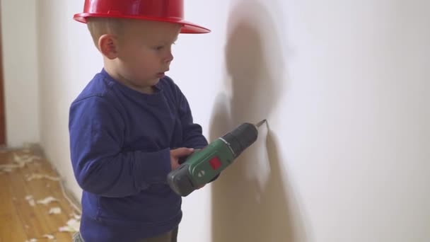 Молодой милый мальчик строитель в форме и каске или шлеме с электрической отверткой на фоне строительства и ремонта . — стоковое видео