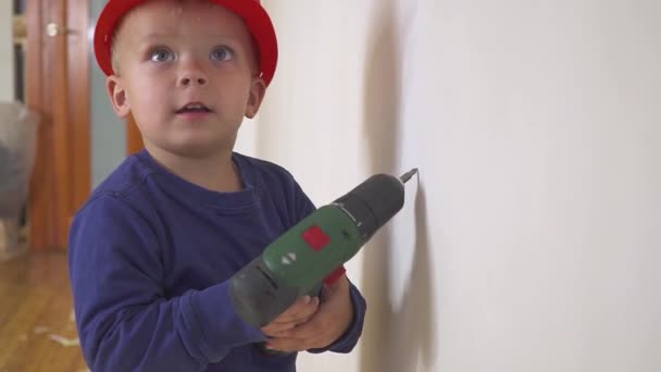 Jonge schattige bouwer jongen in uniform en harde hoed of helm met elektrische schroevendraaier tegen de achtergrond van de bouw en reparatie. — Stockvideo