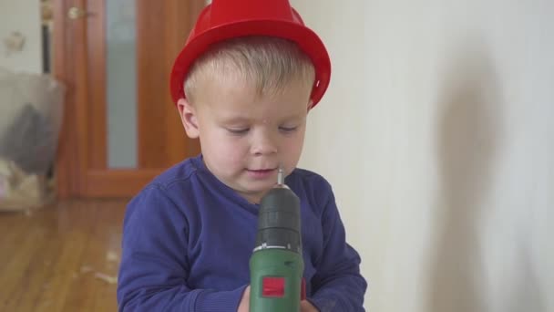 Joven lindo constructor niño en uniforme y casco o casco con destornillador eléctrico contra el fondo de la construcción y la reparación . — Vídeos de Stock