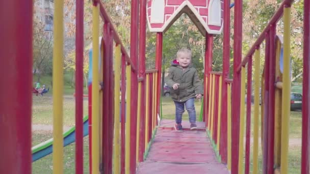 Веселый мальчик бегает по мосту на детской площадке — стоковое видео
