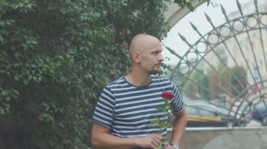 Gülü olan üzgün genç bir adam, geç kalmış bir kadını bekliyor.