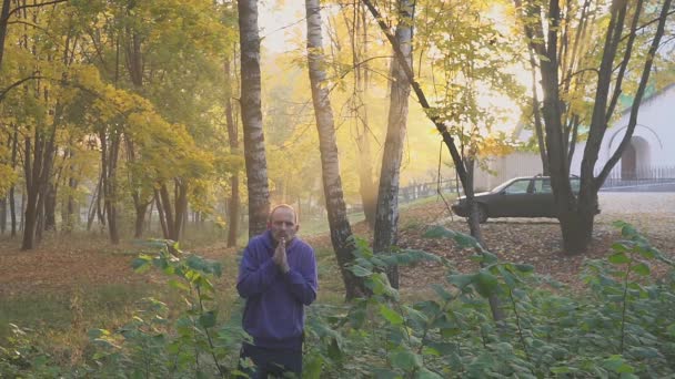 El hombre se congela en el parque de otoño, calentando las manos. fríamente . — Vídeo de stock