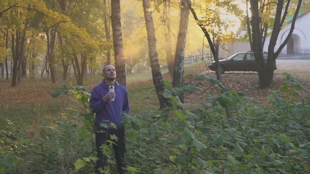 Jongeman thee of koffie drinken uit een thermocup in de herfst park — Stockvideo