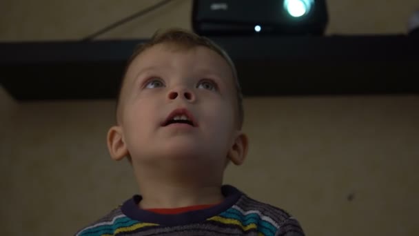 Primer plano de un niño de dos años está viendo la televisión en una habitación oscura . — Vídeos de Stock