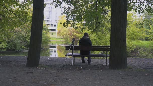 Injured Man with crutches sitting on a bench in the autumn Park — Stock Video