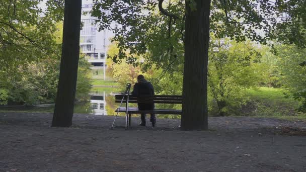 Pria terluka dengan kruk duduk di bangku di taman — Stok Video