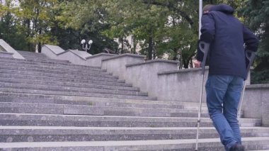 Koltuk değnekli adam merdivenleri çıkıyor. Beton merdiven. Kapsayıcı bir toplum ve bariyersiz bir çevre kavramı