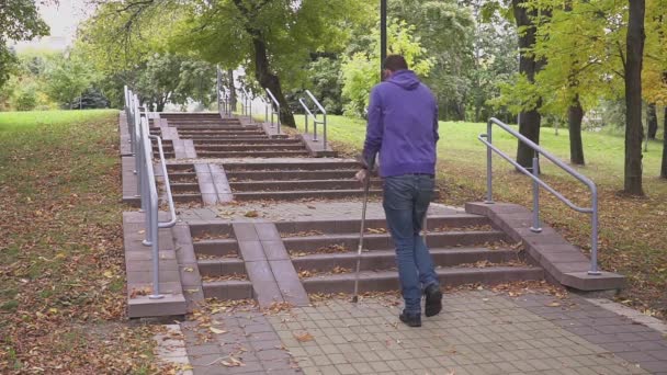 Seorang pria dengan tongkat penopang menaiki satu set tangga. Konsep pada masyarakat inklusif dan lingkungan bebas hambatan — Stok Video
