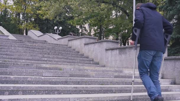 Man on crutches climbs a set of stairs. concrete staircase. Concept on an inclusive society and a barrier-free environment — Stock Video