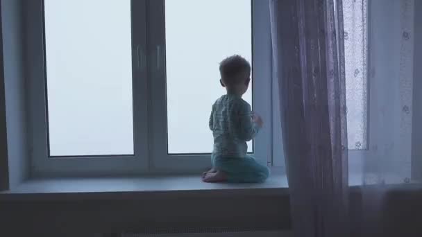 Silueta malého chlapce sedícího u okna na pozadí velkého města s mrakodrapy — Stock video