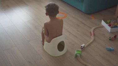 child baby boy toddler sitting on potty in living room, indoors. Toys in the room