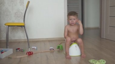 child baby boy toddler sitting on potty in living room, indoors. Toys in the room