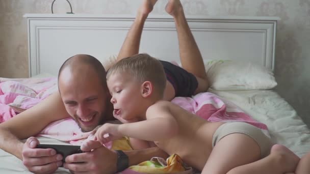 Papa et fils couchés sur le lit et utilisant le téléphone mobile ensemble — Video