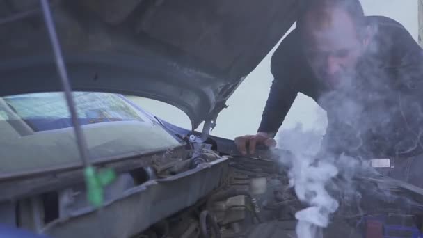 한 남자가 자신의 흡연 자동차 엔진을 평가하려고 하다가 매우 좌절감에 빠져 있다. — 비디오