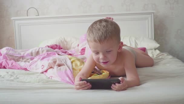 ベッドで3歳の男の子がスマートフォンを使って. — ストック動画