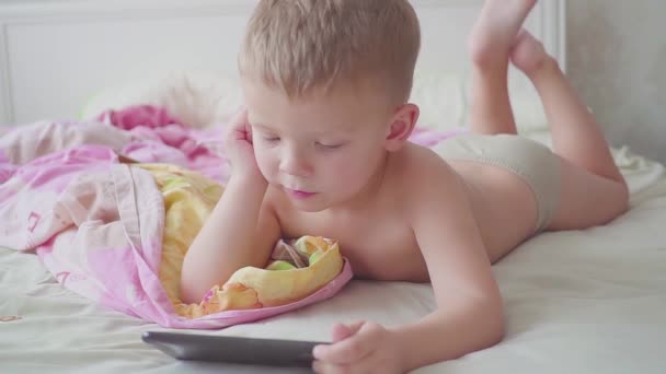 Lustiger dreijähriger Junge im Bett benutzt Smartphone. — Stockvideo