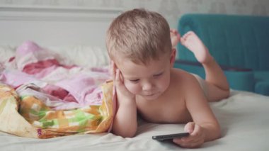 Yatakta üç yaşında bir çocuk akıllı telefon kullanıyor..