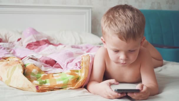 침대에 있는 세 살짜리 남자 아이가 스마트폰을 사용하고 있습니다.. — 비디오