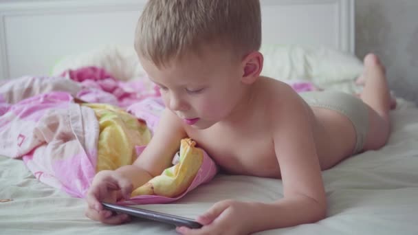 Drie-jarige jongen in bed is met behulp van een smartphone. — Stockvideo