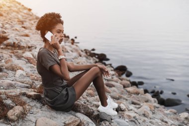 Siyah kız göz kamaştırıcı taşlı bir iskele üzerinde oturan ve cep telefonu üzerinden onun arkadaşı ile konuşurken; genç Afro-Amerikan erkek Nehri yakınında otururken ailesi smartphone üzerinden arıyor
