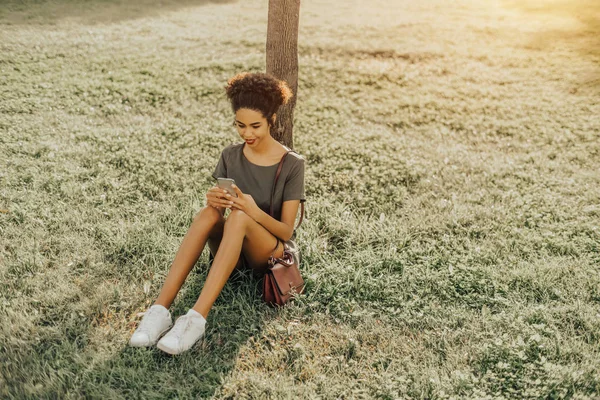 Sweet Smiling Teenage Black Girl Sitting Grass Lawn Typing Message — Stock Photo, Image