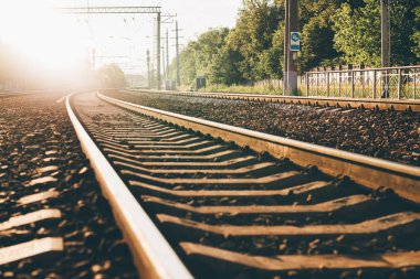 Alt ağaçlar ve sağdaki Beton çit, şose yere, birden çok sütun ve teller yukarıdaki güneş tarafından backlighted tren yolu görünümünü; sıcak güneşli yaz gün