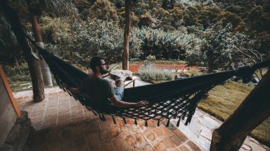 Yakışıklı genç gözlük sakallı adam düşünceli bir kenara açık havada otururken seyir lüks yaz evinin örme hamak tatilinde; yağmur ormanları ve sebebi içinde belgili tanımlık geçmiş