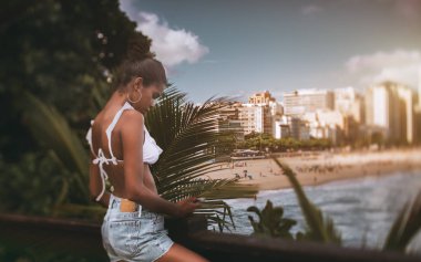 Genç bir sevimli siyah kızın onun smartphone şehir plaj ve kıyı şeridi, kopyalama alanı alanı sağdaki manzaralı iskelede duran sadece filme fotoğrafları kontrol doğru tilt-shift vurdu