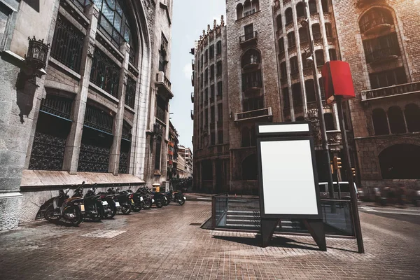 Vertical empty billboard placeholder template on the street with multiple motorbikes and subway entrance behind; blank advertising banner mockup in urban settings surrounded by historical buildings